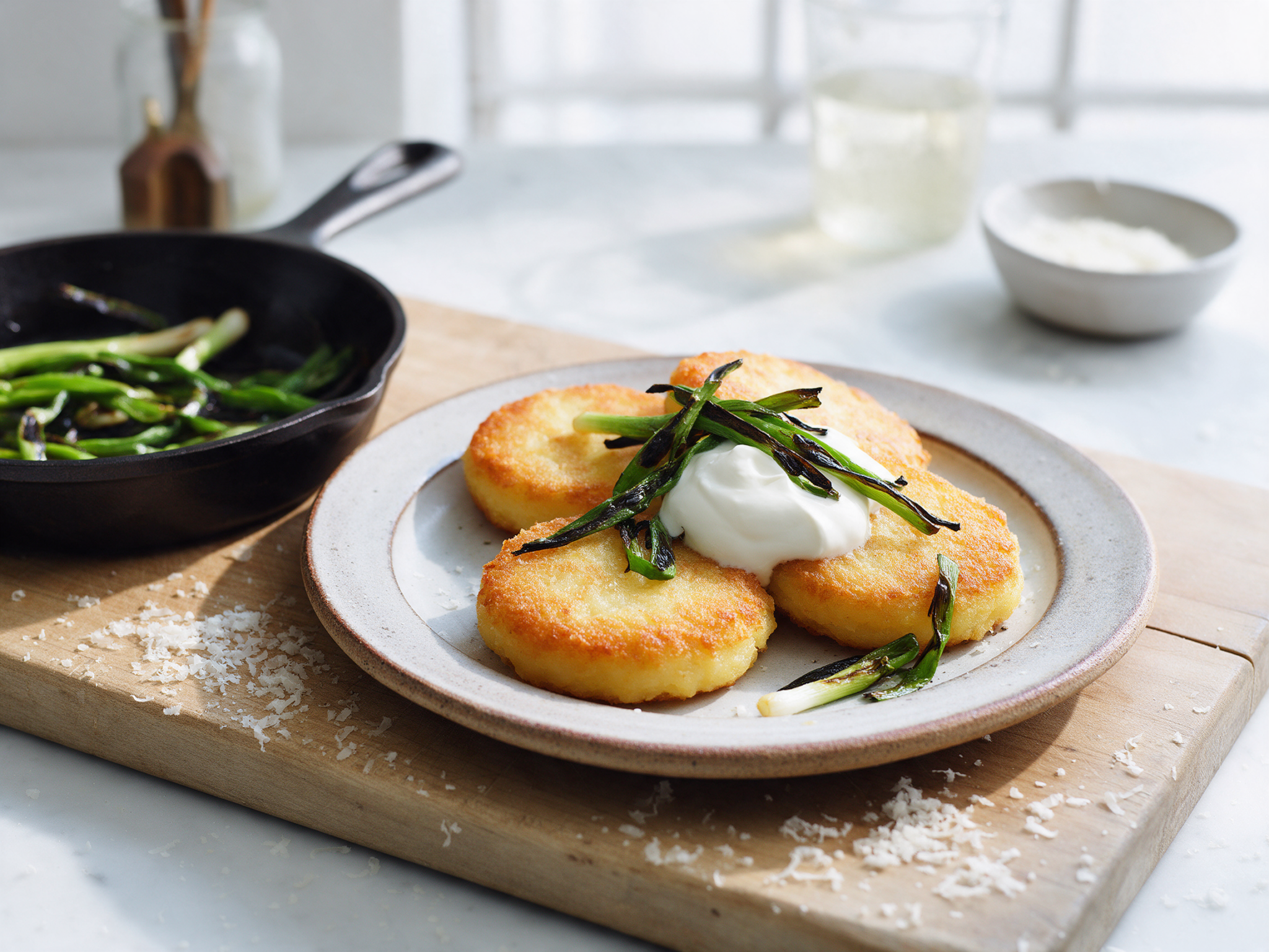 Crisp potato cakes topped with sour cream and charred spring onions on a stoneware plate